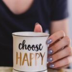 selective focus photography of person touch the white ceramic mug with choose happy graphic